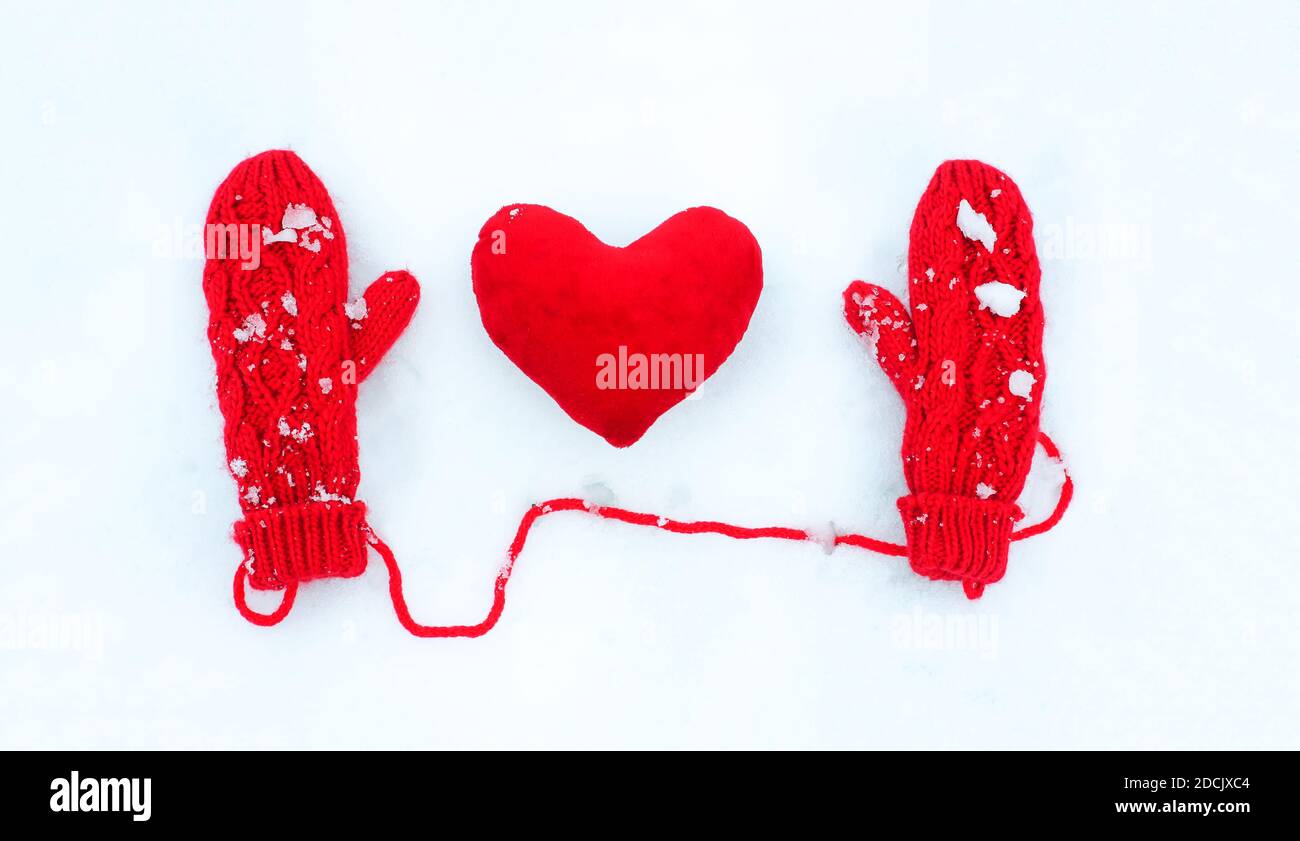 Rote Handschuhe und Plüsch dekorative Herzen auf der Schneeoberfläche. Stockfoto