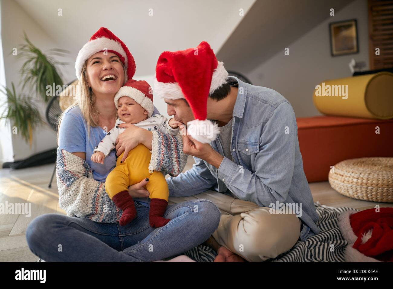 Glücklicher junger Vater küsst die Hand eines Babys in den Armen der Mutter, lacht, trägt santa Hüte Stockfoto