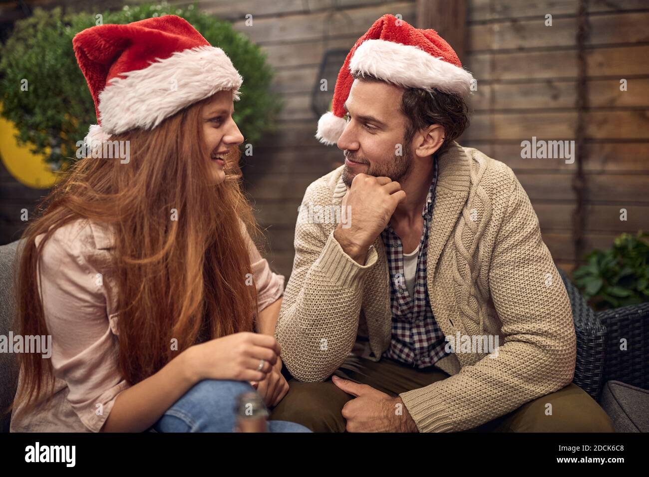Junges erwachsenes Paar, das am Silvesterabend mit Weihnachtsmützen spricht, flirtet, lächelt. Corona, covid Konzept Stockfoto