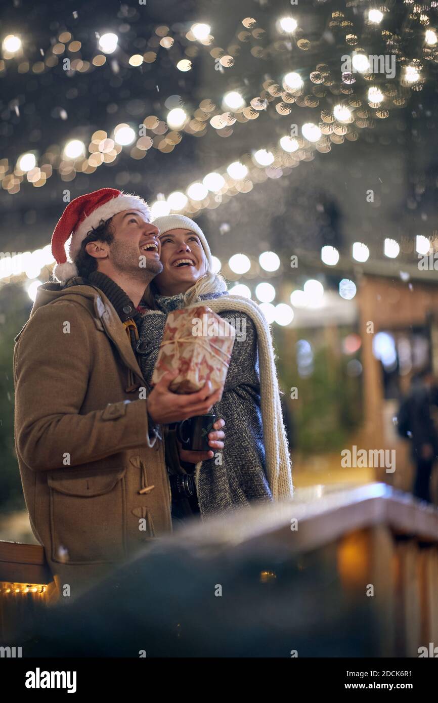 Ein junges glückliches Paar in der Liebe beobachten Schneefall in einer magischen Nacht auf weihnachtsfest in der Stadt. Festival, Liebe, Beziehung, Weihnachten, Schnee Stockfoto