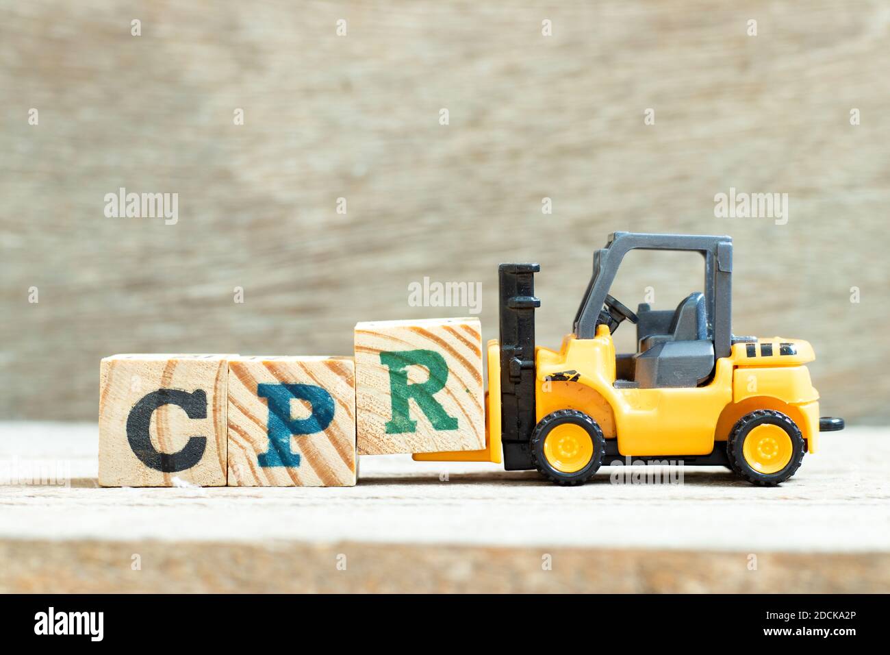 Spielzeug Gabelstapler halten Buchstabenblock R, Wort CPR (Abkürzung von Cardiopulmonary Reanimation) auf Holzhintergrund zu vervollständigen Stockfoto