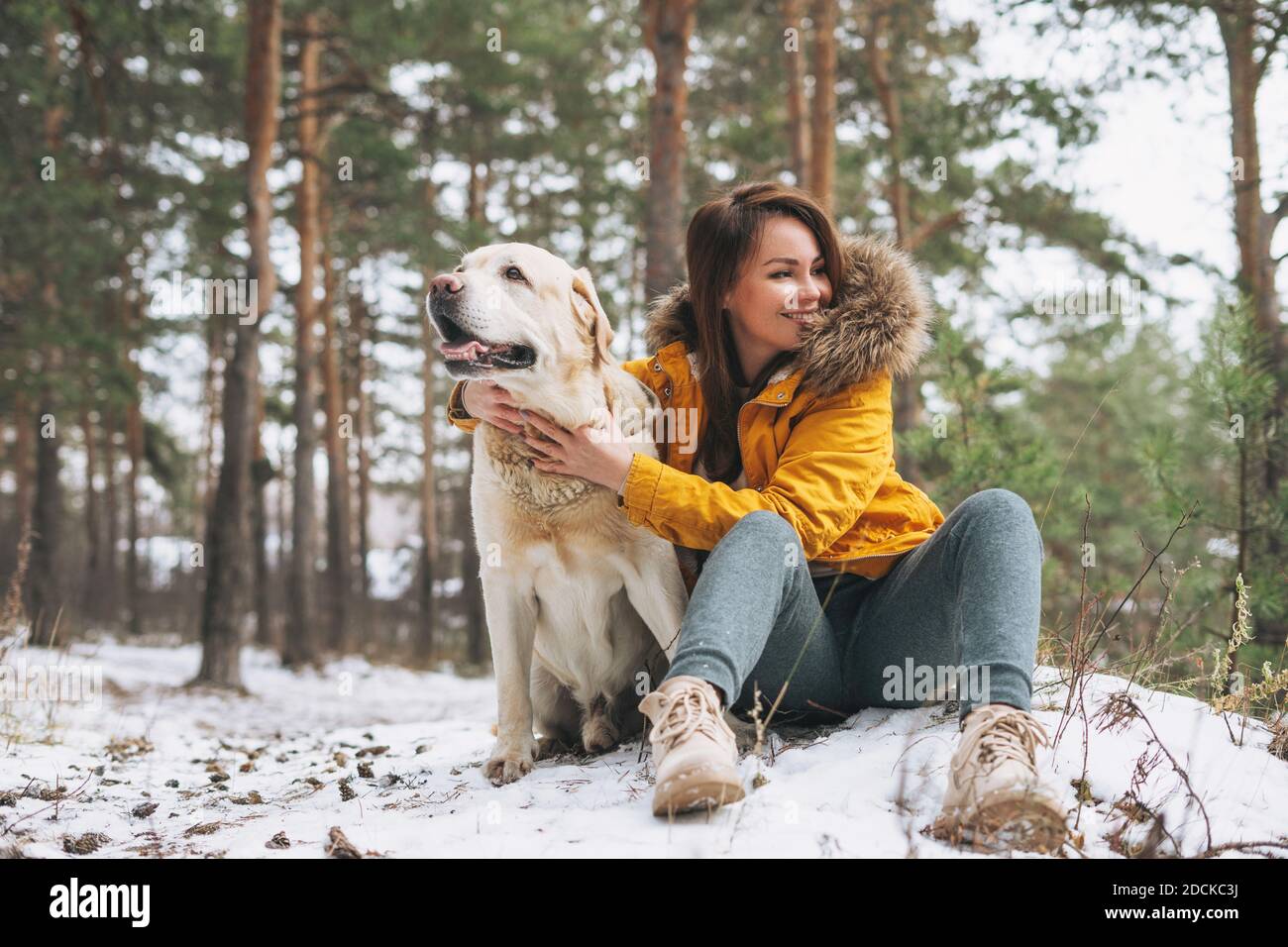 Junge lächelnde Frau in gelber Jacke mit großen Art weiß Hund Labrador Wandern im Winterwald Stockfoto