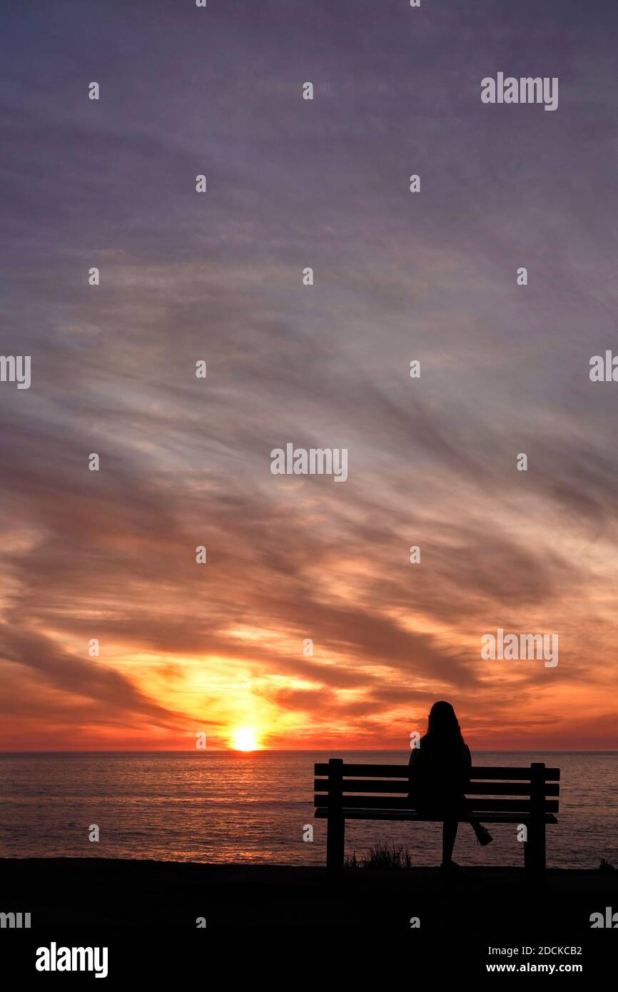 San Diego, Kalifornien, USA. November 2020. Eine Frau sitzt während des Sonnenuntergangs am Windansea Beach in La Jolla auf einer Bank. Mit COVID-19 Infektionen in ganz Kalifornien, Gov. Gavin Newsom gab eine nächtliche Ausgangssperre aus, die "unwesentliche" Aktivitäten und Versammlungen zwischen 10 Uhr und 5 Uhr Verbot.Kredit: K.C. Alfred/ZUMA Wire/Alamy Live News Stockfoto