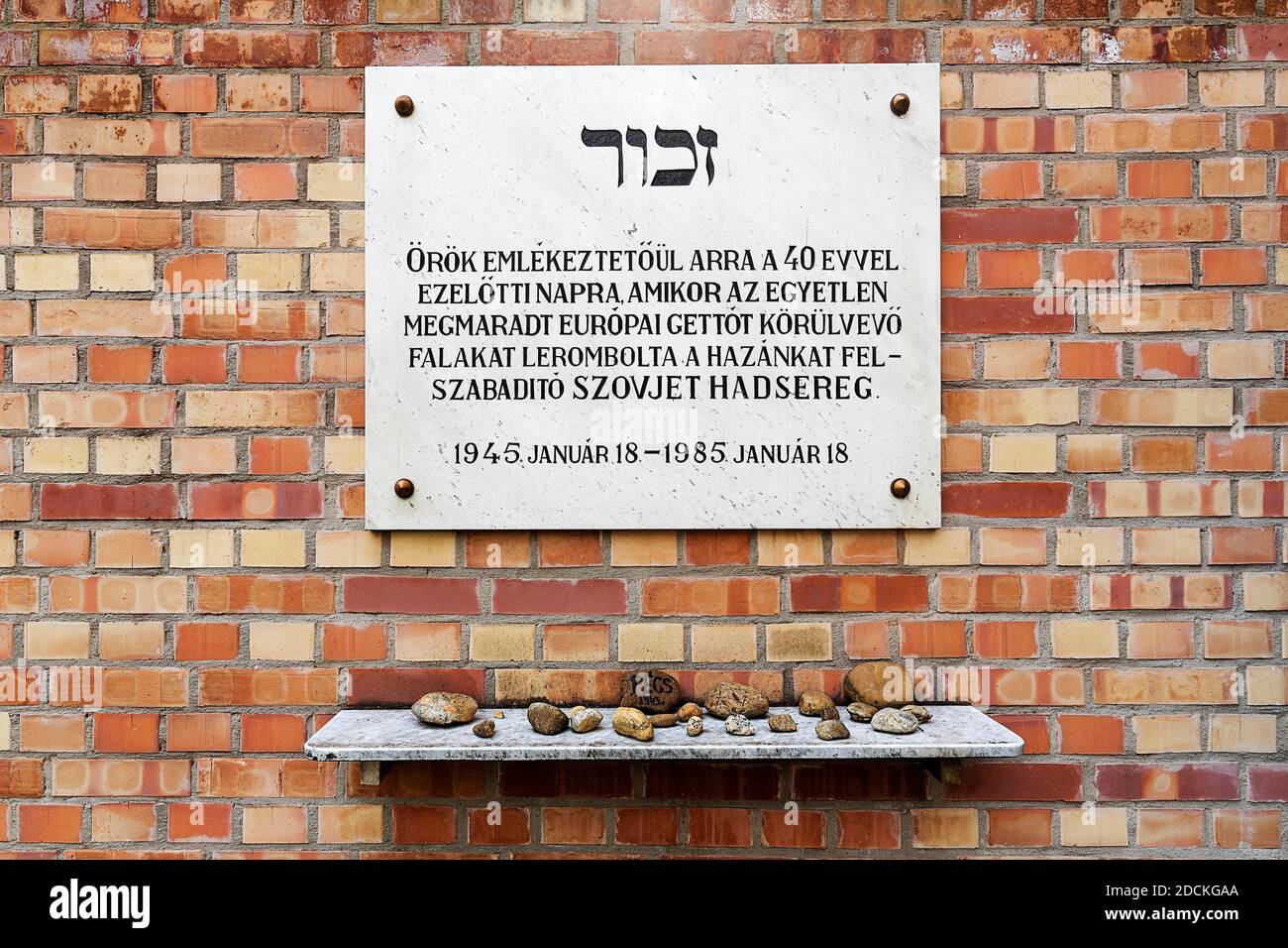 Gedenktafel für die Befreiung des jüdischen Ghettos an einer Wand aus roten Ziegeln, mit Steinen, die auf einer Marmorplatte darunter abgelegt sind, groß Stockfoto