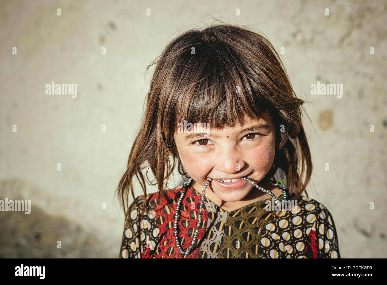 Mädchen mit kurzem Pony, sie hat ihre Kette im Mund, Ishkashim, Afghanistan Stockfoto