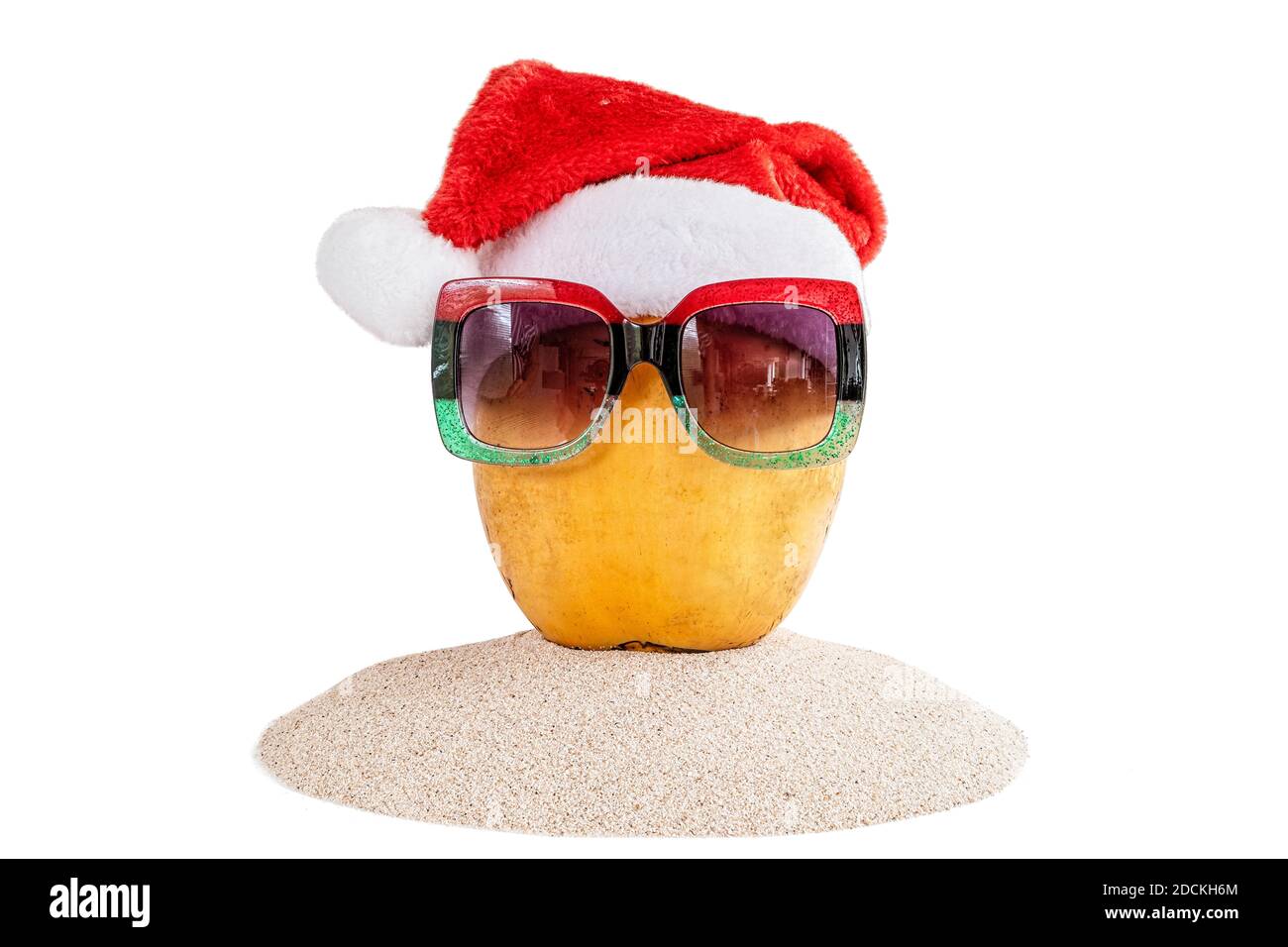 Frische gelbe Kokosnuss in einem roten Weihnachtsmütze mit roter und grüner Sonnenbrille, auf Sand. Stockfoto