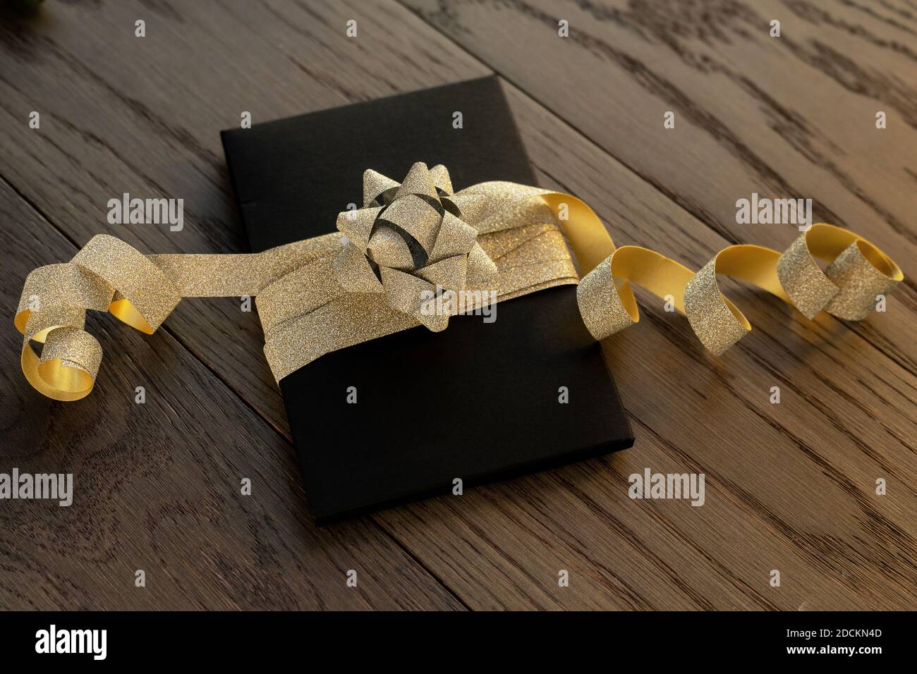 Nahaufnahme der Gegenwart auf einem hölzernen Vintage-Tisch. Schwarze Box mit goldener Schleife. Vorbereitung auf Weihnachten, Geburtstag oder andere Feiertage und Feiern. Stockfoto