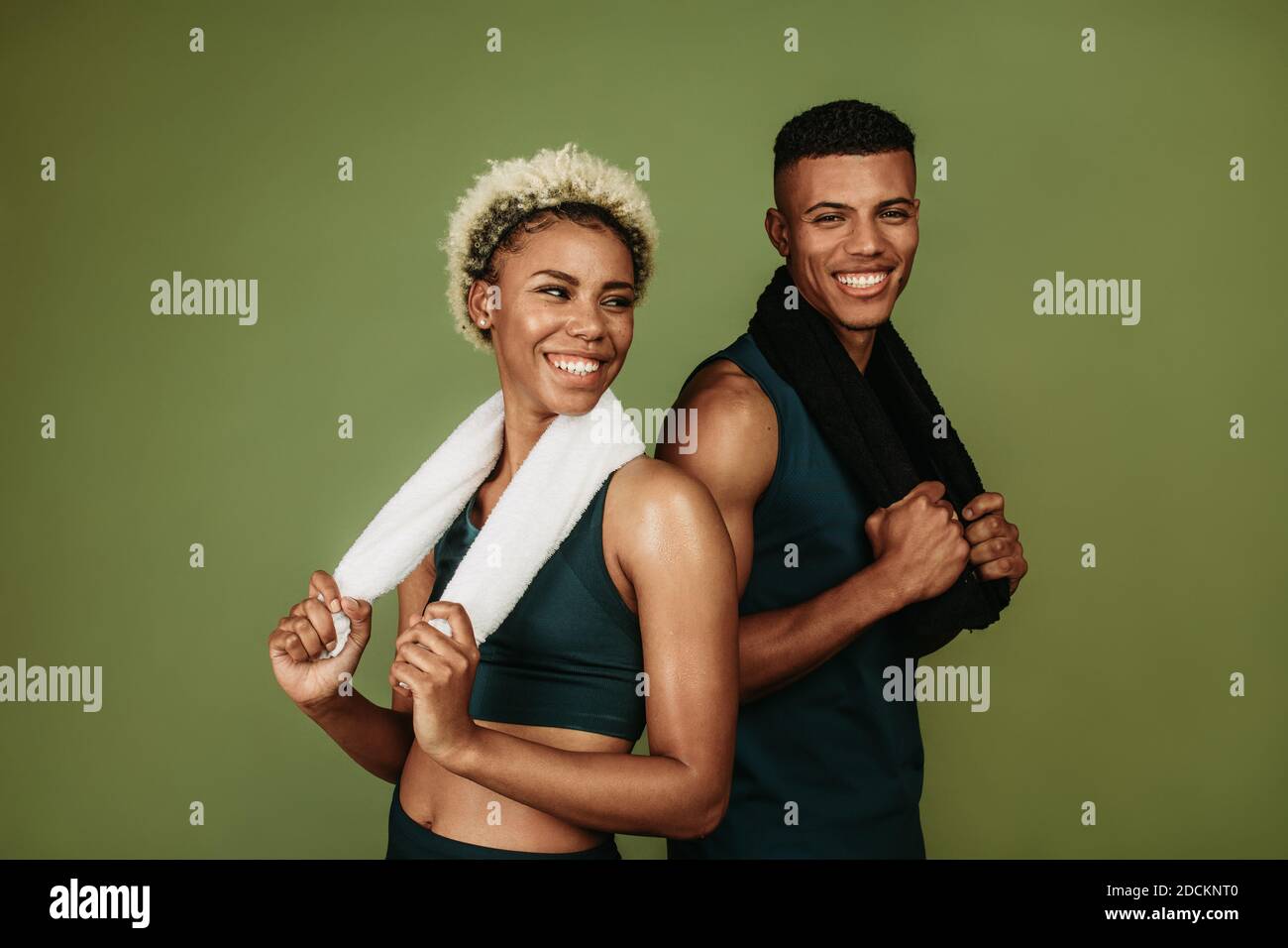 Lächelndes afroamerikanisches Fitnesspaar, das sich nach dem Workout entspannt. Fitness-Mann und -Frau stehen zusammen und halten Handtücher auf grünem Hintergrund. Stockfoto