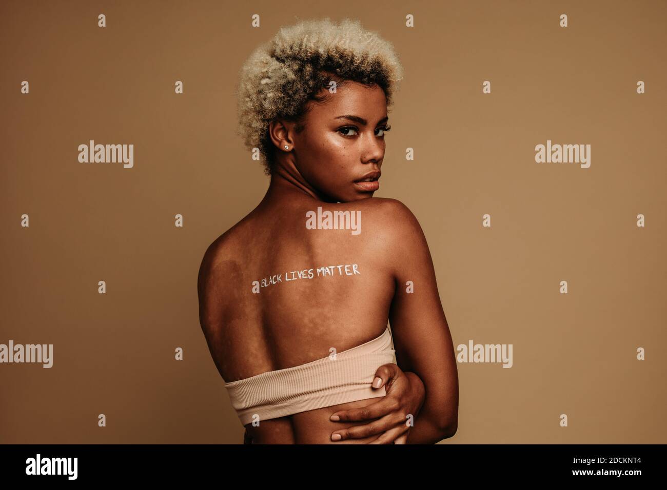 Rückansicht der Frau, die auf braunem Hintergrund steht, mit Wörtern, die schwarze Leben Materie auf Rückseite geschrieben haben. afroamerikanische Frau, die Antirassismus-Ansichten ausdrückt. Stockfoto