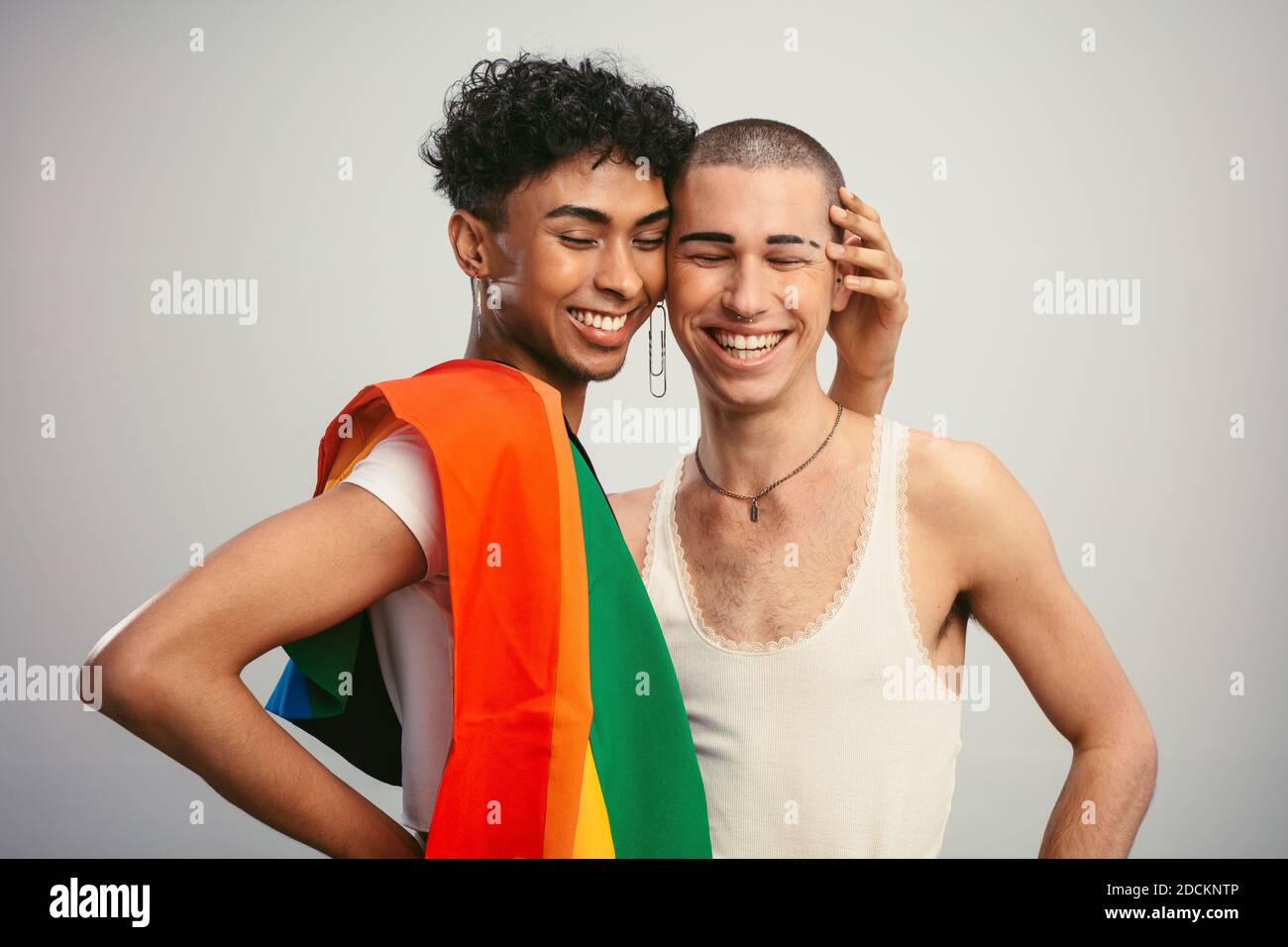Fröhliche Homosexuell Paar mit Stolz Flagge auf weißem Hintergrund. Zwei homosexuelle Männer stehen zusammen und lächeln. Stockfoto