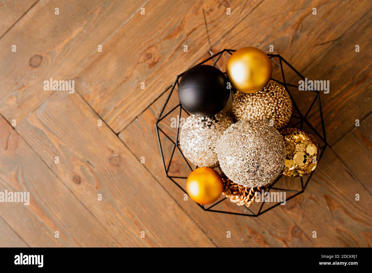 Goldene, beige und schwarze glänzende Kugeln für Weihnachtsdekor in einem schwarzen Metallkorb auf einem Holzdeckel. Weihnachtskarte, selektiver Fokus Stockfoto