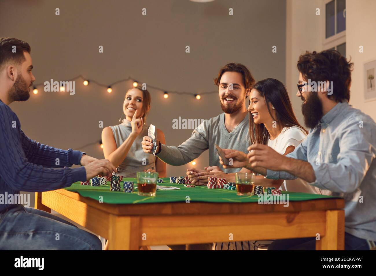 Eine Gruppe von spielenden Freunden sitzen zu Hause an einem Tisch und spielen Poker, während sie den Abend genießen. Stockfoto
