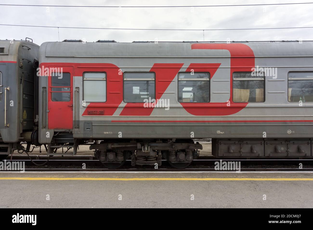 Das Logo RZD einer großen staatlichen russischen Eisenbahngesellschaft ist auf einem grauen Wagen eines Personenzuges auf dem Bahnsteig der Stadt Barabinsk gezeichnet. Stockfoto