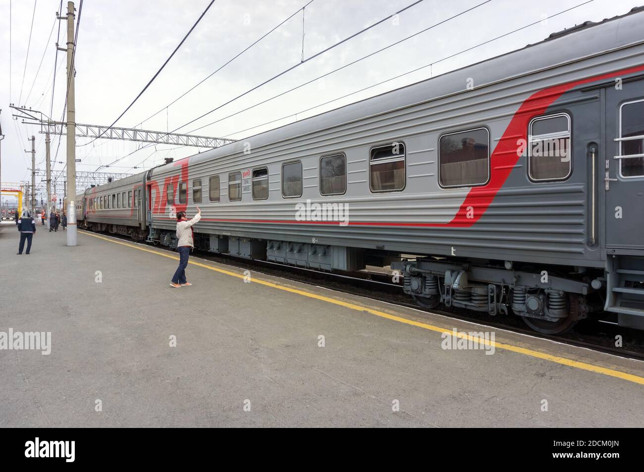 Frau steht neben dem Zug der Russischen Eisenbahn auf dem Bahnsteig des Bahnhofs Barabinsk, der sich auf der berühmten Transsibirischen Eisenbahn befindet. Stockfoto