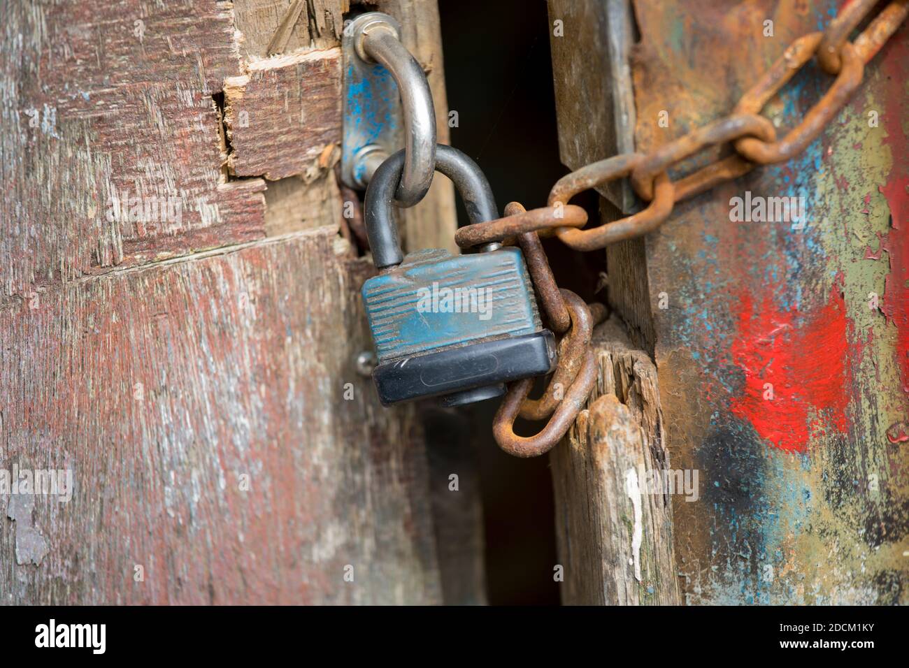Ein altes Vorhängeschloss, das zwei Türen einer alten Scheune verschließt. Die Türen sind rot, blau und grün gestrichen und rostig. Stockfoto