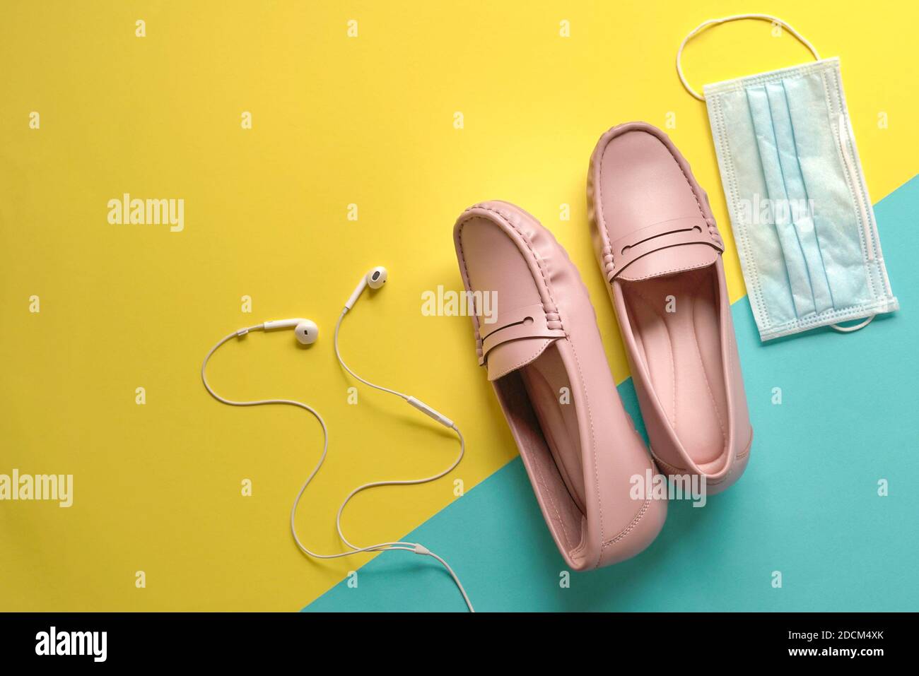 Stilvolle Damenschuhe, Ohrhörer und medizinische Gesichtsmaske auf gelbem und blauem Hintergrund. Wandern im Freien mit Schutz vor Viren-Konzept. Stockfoto