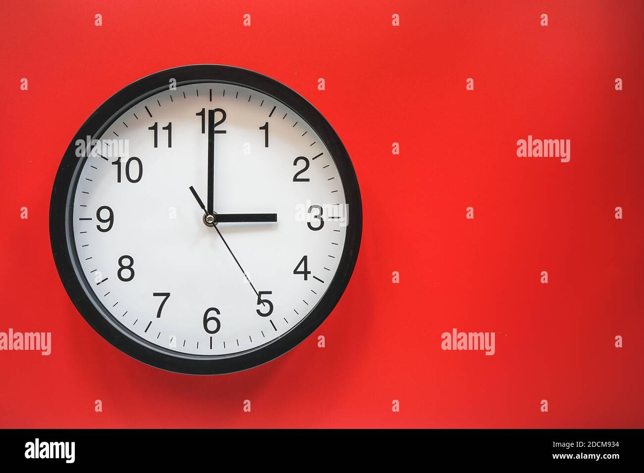 Klassische schwarz-weiße Analoguhr auf rotem Hintergrund bei Drei Uhr mit Kopierplatz Stockfoto