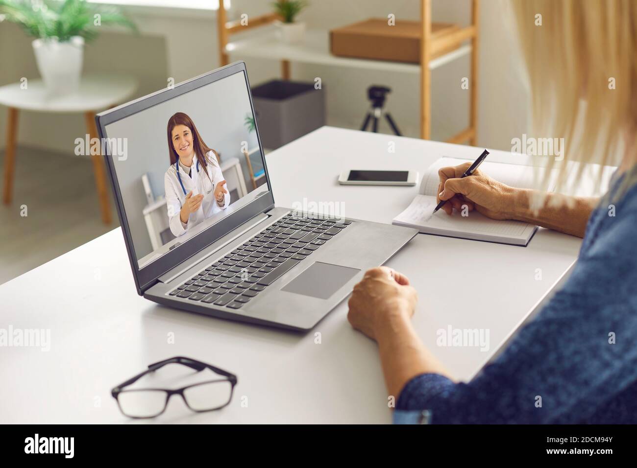 Reife Frau Notizen beim Hören auf einen Online-Arzt Gesundheitsberatung Stockfoto