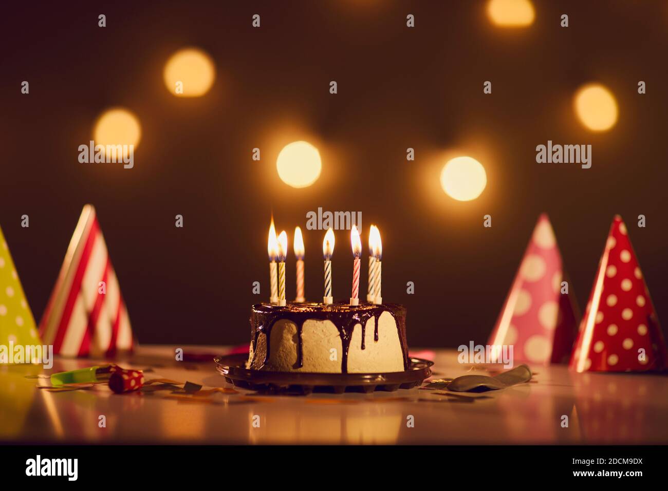 Geburtstagskuchen mit Schokolade Ganache und brennenden Kerzen auf Tisch mit Partyhüten Stockfoto