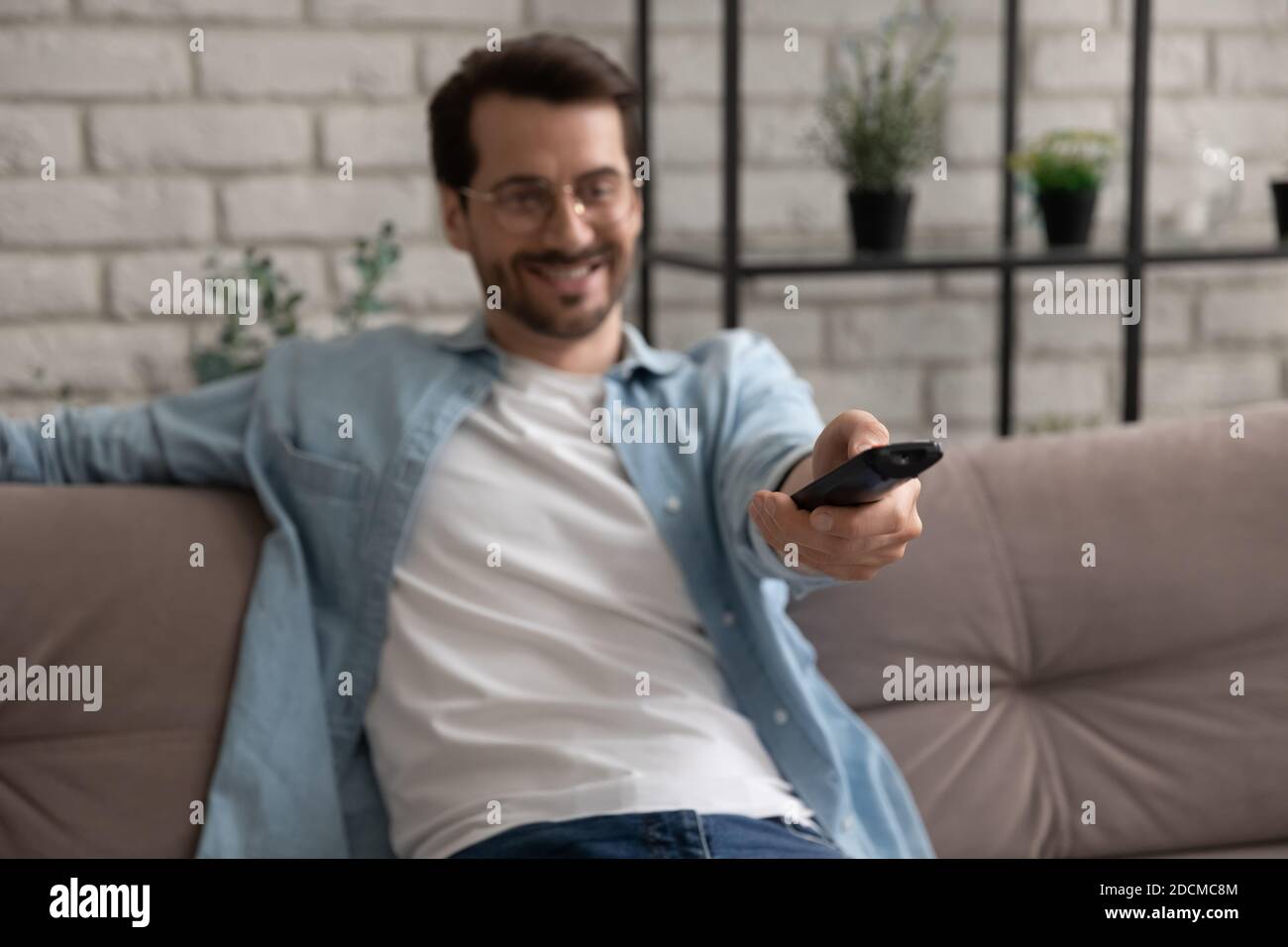 Glücklicher junger Mann, der Kanäle auf Smart tv umschaltet, mit Controller. Stockfoto