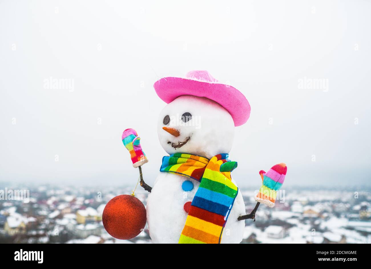 Schneemfrau mit Weihnachtsspielzeug. Schneemann hält Neujahr Ball. Schneemann in rosa Hut. Weihnachten. Lustiger Schneemann. Frohe Weihnachten und ein glückliches neues Jahr Stockfoto