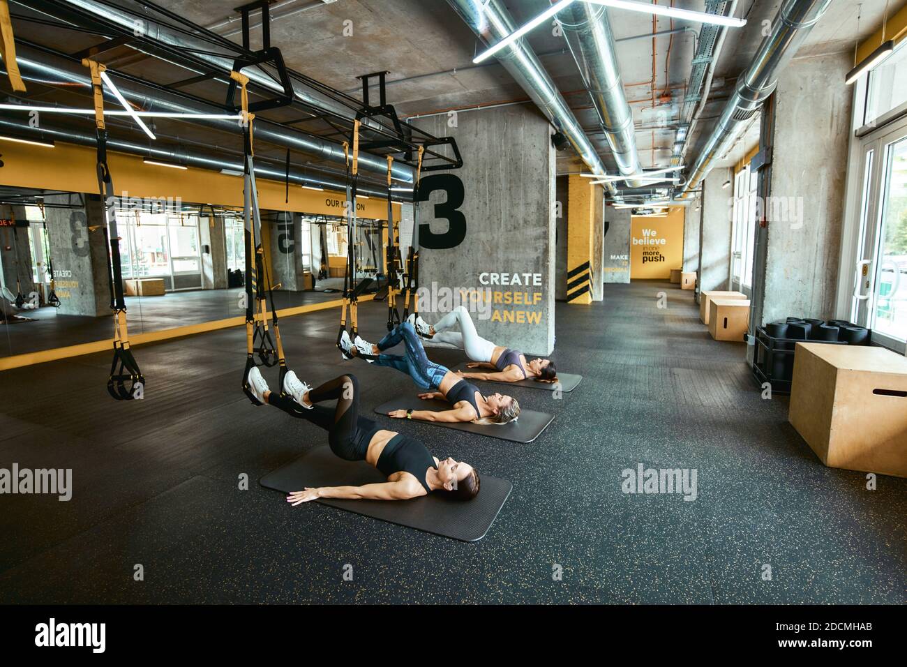 Krafttraining. Drei junge kaukasische Sportlerinnen in Sportbekleidung trainieren mit Fitness trx Straps im Industrial oder Crossfit Gym. Sport, Menschen arbeiten, Wellness und gesunde Lebensweise Stockfoto