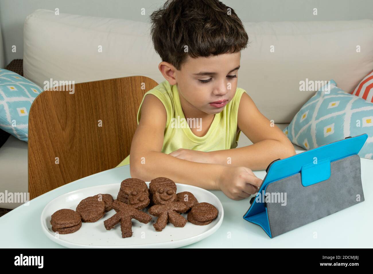 Kind in Quarantäne, Kekse essen und mit seinem Tablet herumbasteln. Stockfoto
