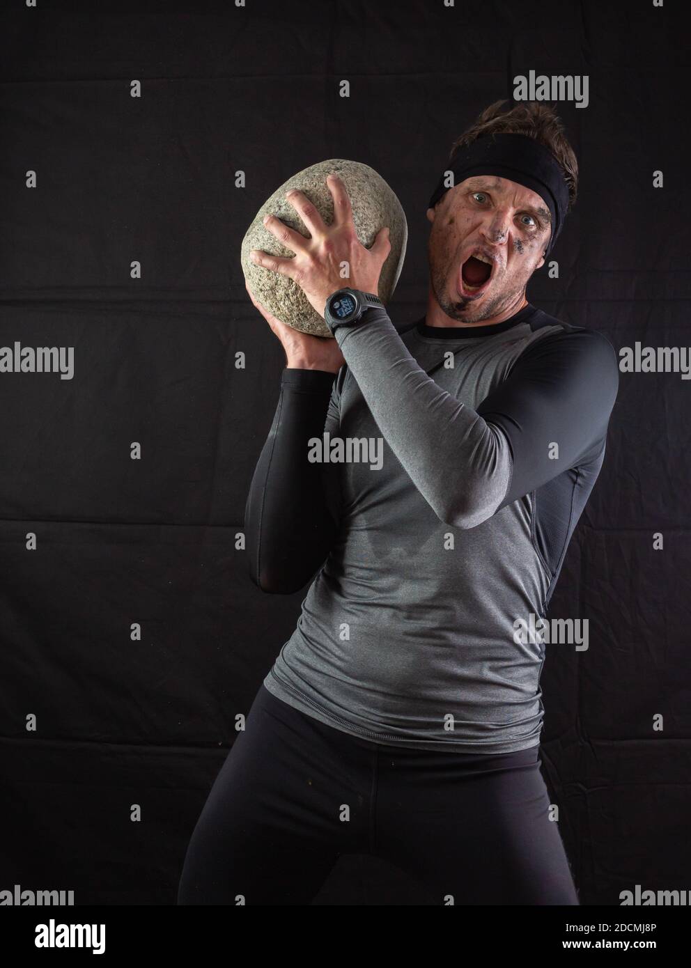Sportlicher Mann, der einen großen schweren Stein in den Händen hält Auf schwarzem Hintergrund Stockfoto