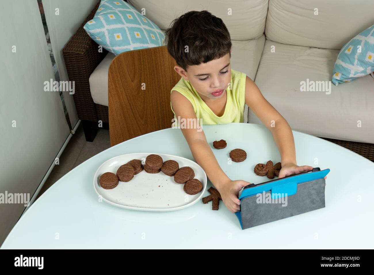 Kind in Quarantäne, Kekse essen und mit seinem Tablet herumbasteln. Stockfoto