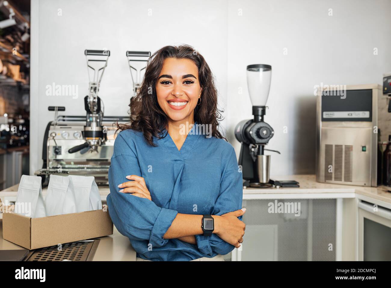 Lächelnder Besitzer des Cafés, der die Kamera mit gekreuzten Armen ansah. Junge Unternehmerin, die in einem Café am Tisch steht. Stockfoto