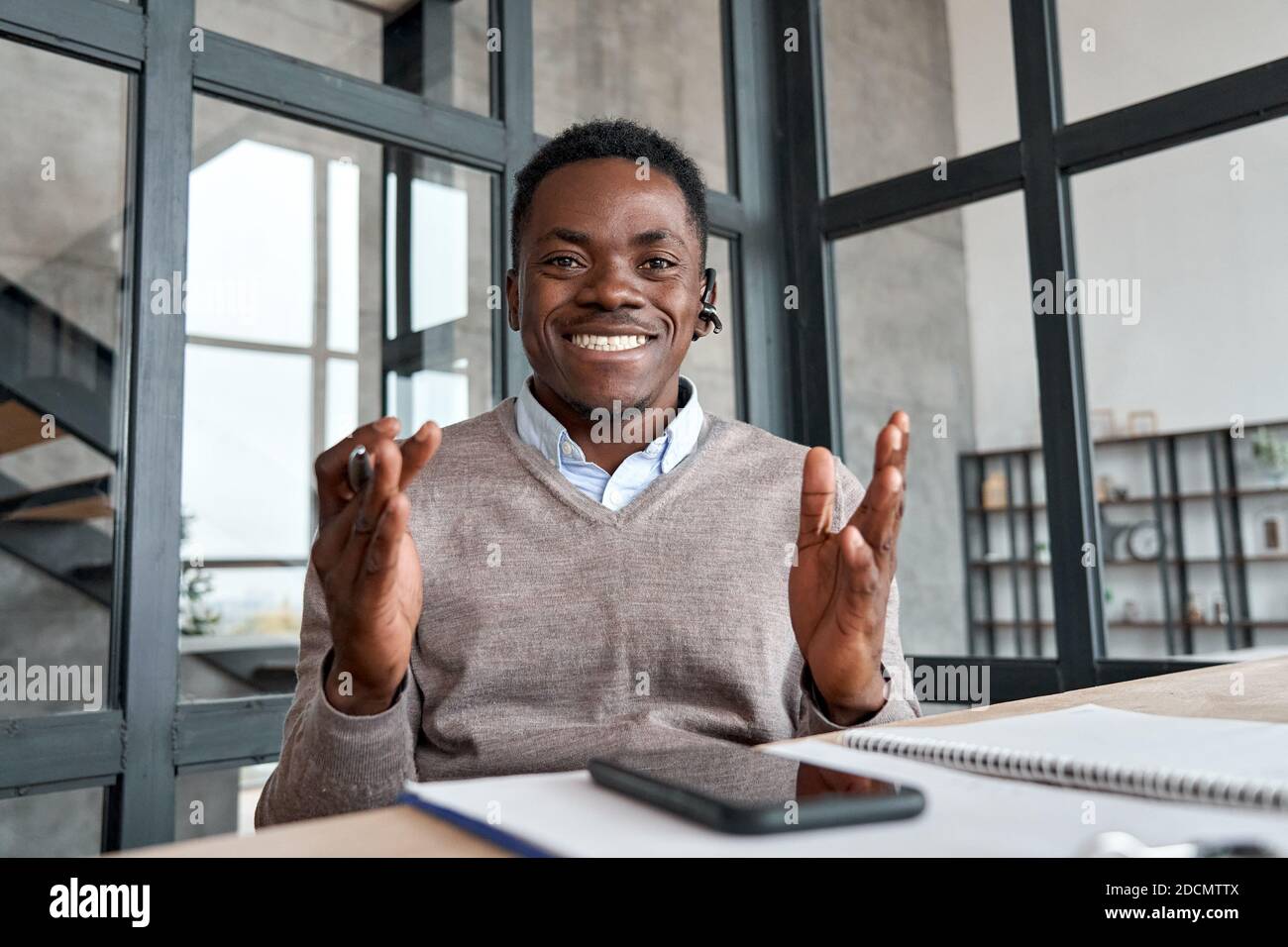 Glücklicher afrikanischer Geschäftsmann, der ein Headset trägt und mit der Kamera spricht, mit der Webcam. Stockfoto