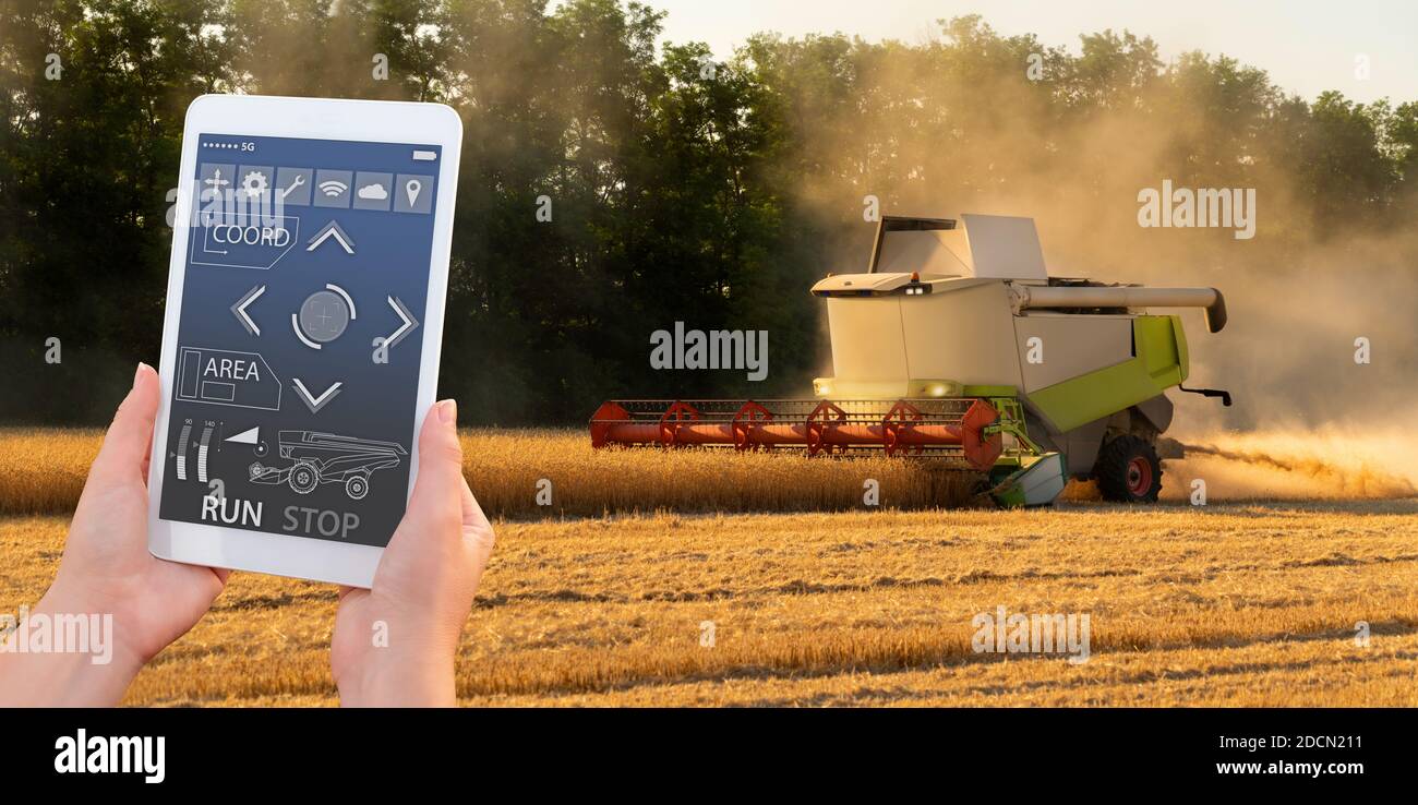 Farmer verwendet ein digitales Tablet, um den autonomen Erntemaschinen zu steuern. Smart Farming-Konzept Stockfoto