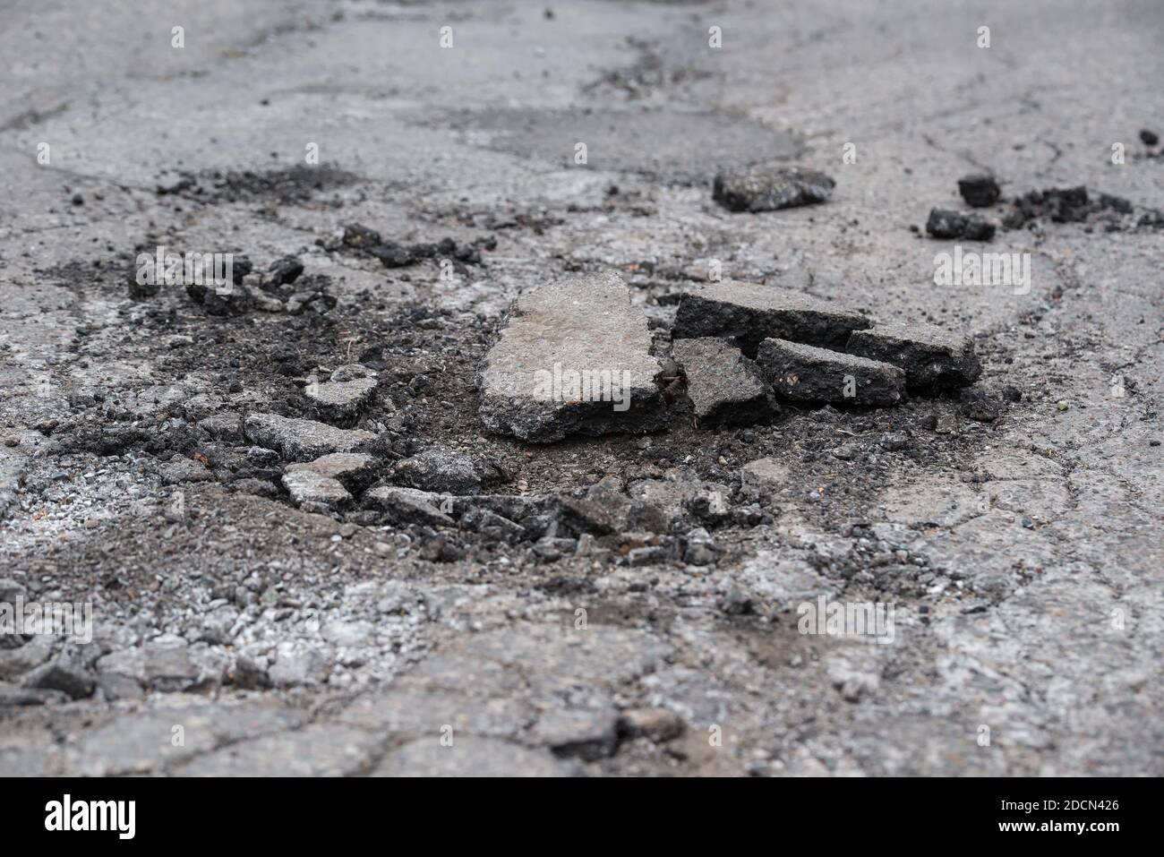 Eine raue, kaputte Fahrbahn. Stücke von gebrochenem Asphalt liegen in einem Loch in der Straße. Die Straße ist geflickt und geknackt. Stockfoto
