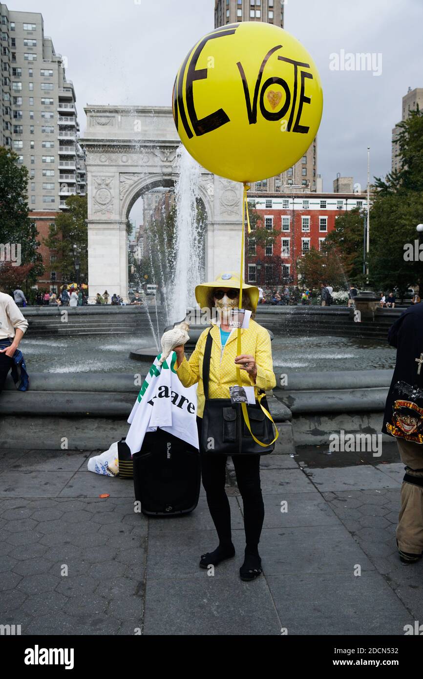 NEW YORK - 24. Oktober 2020: Ältere Frau mit einem gelben Ballon mit der Aufschrift "Vote". Sie ist in Gelb gekleidet und hält eine Muschelschale. Stockfoto