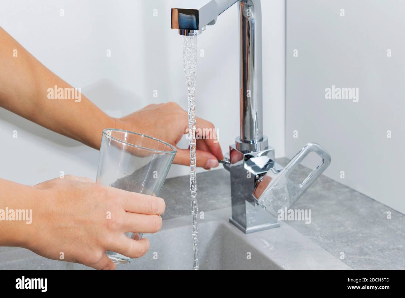 Hand hält ein Glas Wasser aus der Küche gegossen Wasserhahn Stockfoto