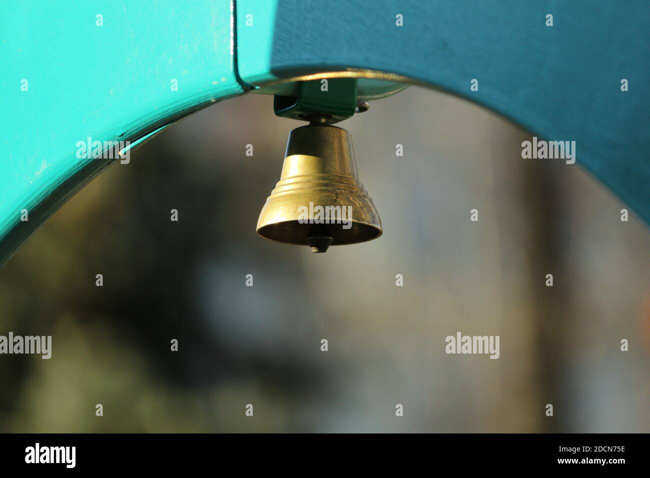 Die Bronzeglocke leuchtet in der Sonne. Metallic Bronze gelb goldene Glocke auf einer blauen Holzstruktur im Freien Sonnenlicht. Stockfoto