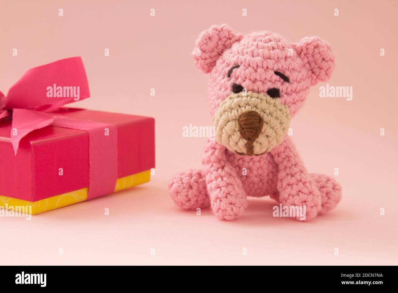 Kleiner Häkelbär in pink mit einer Geschenkbox auf der Rückseite. Rosa Farbe. Liebeskonzept. Stockfoto