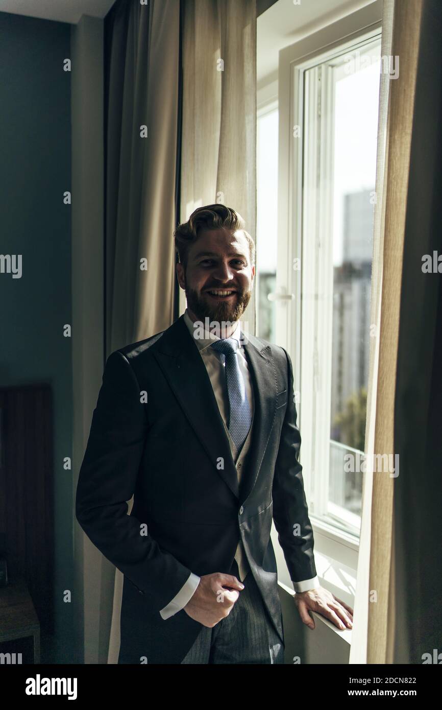 Ein flacher Fokus eines erwachsenen Mannes mit Bart In einem eleganten Anzug und in der Nähe der Fenster Stockfoto