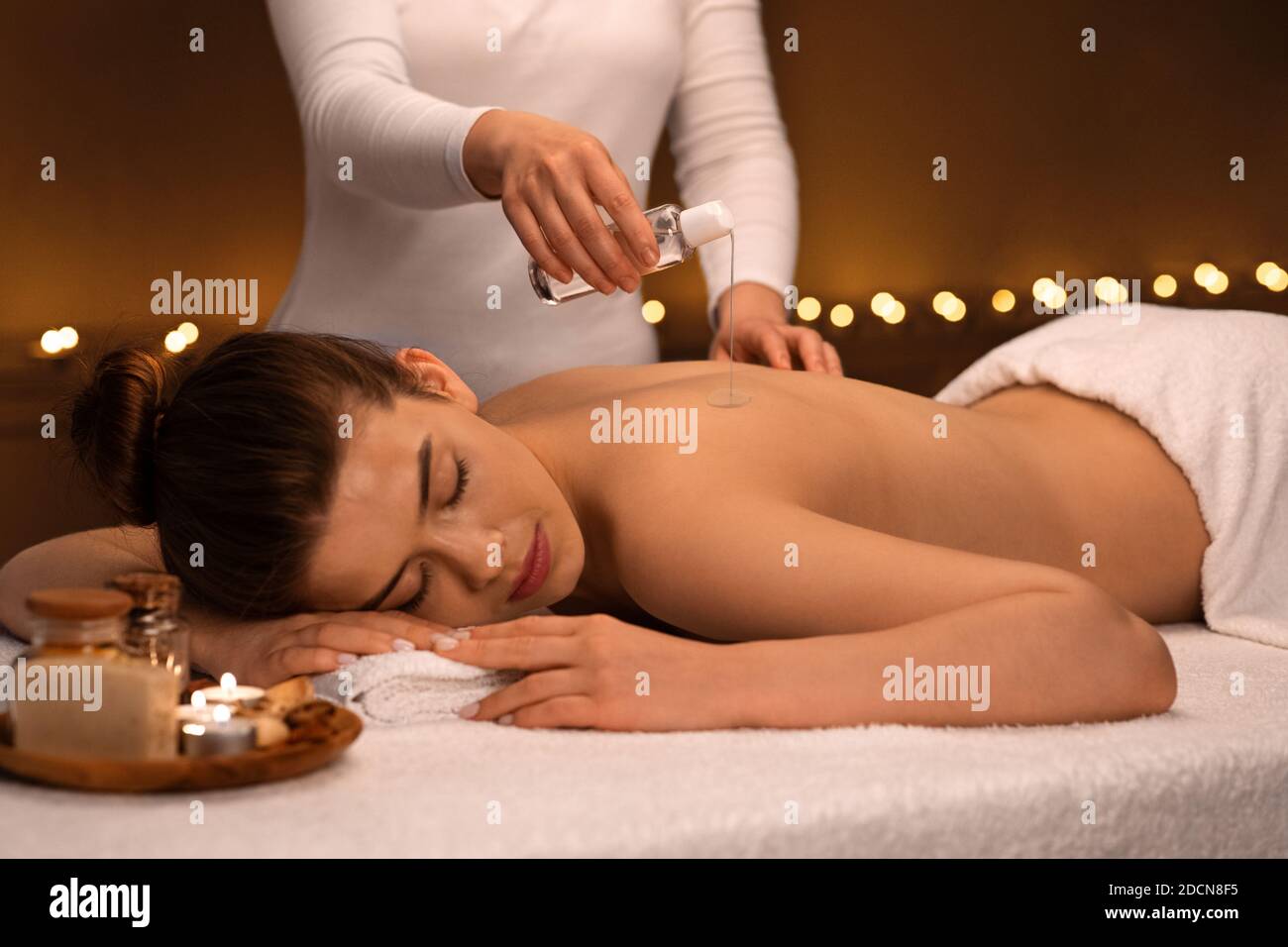 Massage Therapeut gießt Öl auf junge Frau zurück Stockfoto