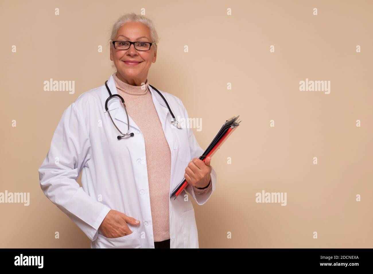 Lächelnde leitende Ärztin mit Stethoskop um den Hals, die Papiere hält. Studioaufnahme Stockfoto