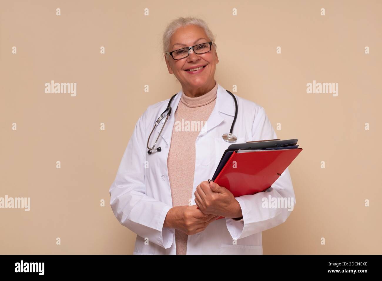 Lächelnde leitende Ärztin mit Stethoskop um den Hals, die Papiere hält. Studioaufnahme Stockfoto