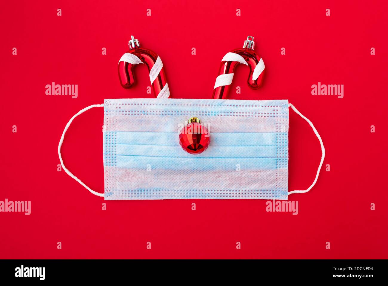 Festliches Coronavirus weihnachtskonzept aus Gesichtsmaske und Dekorationen auf rotem Hintergrund. Flach liegend. Draufsicht Stockfoto