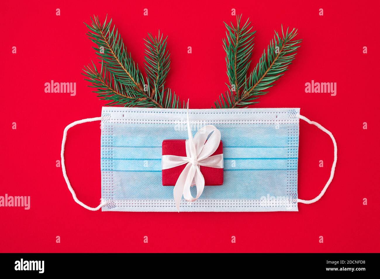 Coronavirus weihnachtskonzept aus Gesichtsmaske, Tannenbaum, Geschenkbox und Dekorationen auf rotem Hintergrund. Flache Lage. Draufsicht Stockfoto