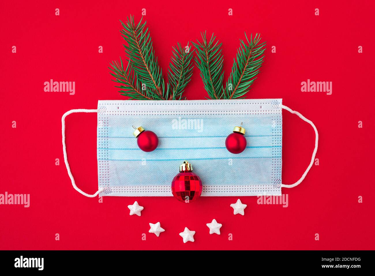 Festliches Coronavirus weihnachtskonzept aus Gesichtsmaske, Tannenbaum und Dekorationen auf rotem Hintergrund. Flache Lage. Draufsicht Stockfoto