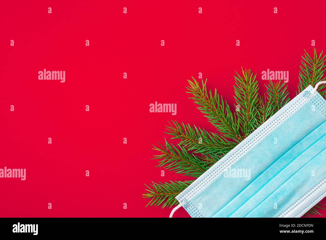 Weihnachtshintergrund während der Pandemie von Covid 19 aus Gesichtsmaske und Tannenbaum auf rotem Hintergrund. Flache Lage. Draufsicht mit Kopierraum Stockfoto