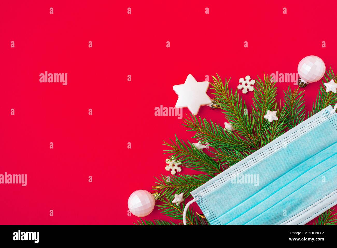 Festliches Coronavirus weihnachtskonzept aus Gesichtsmaske, Tannenbaum und Dekorationen auf rotem Hintergrund. Flach liegend. Draufsicht mit Kopierraum Stockfoto