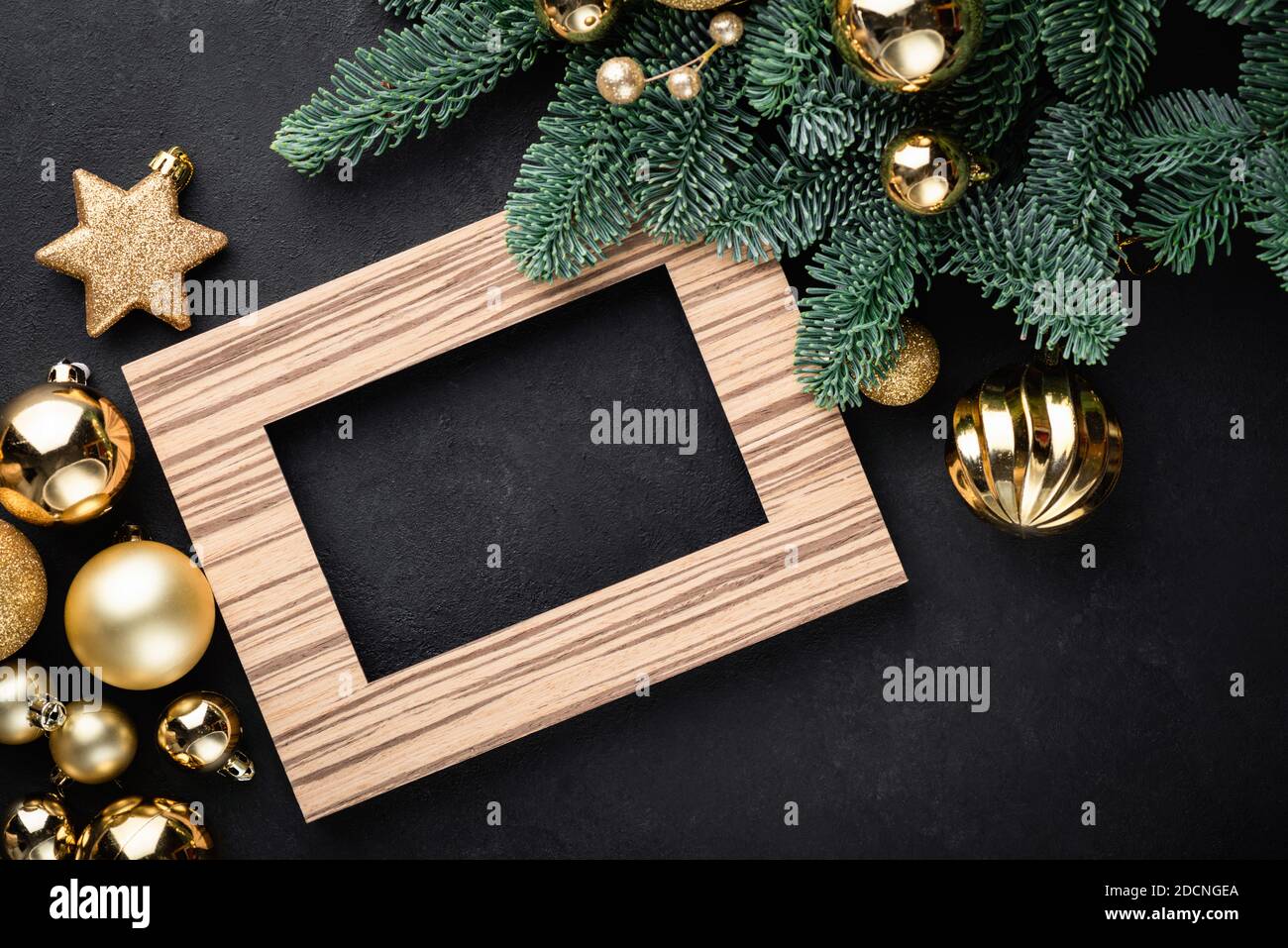 Weihnachts- oder Neujahrshintergrund mit leerem Fotorahmen, Tannenbaum und goldenem Weihnachtsspielzeug auf schwarzem Hintergrund Stockfoto