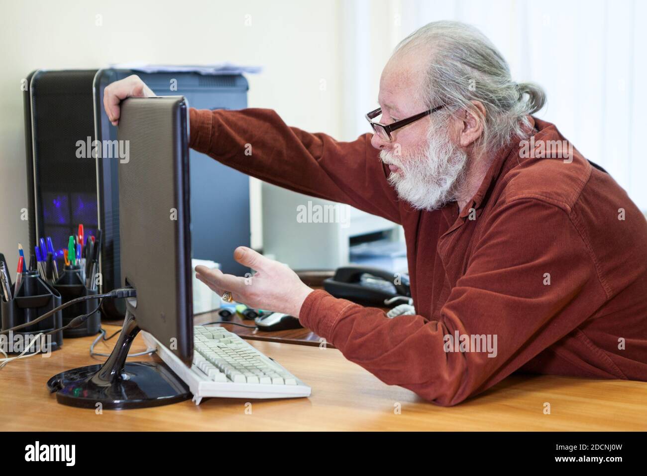 Serious Senior Mann versucht, Computer zu verwenden, hält Monitor mit Verständnis. Ältere Menschen mit neuer Technologie Stockfoto