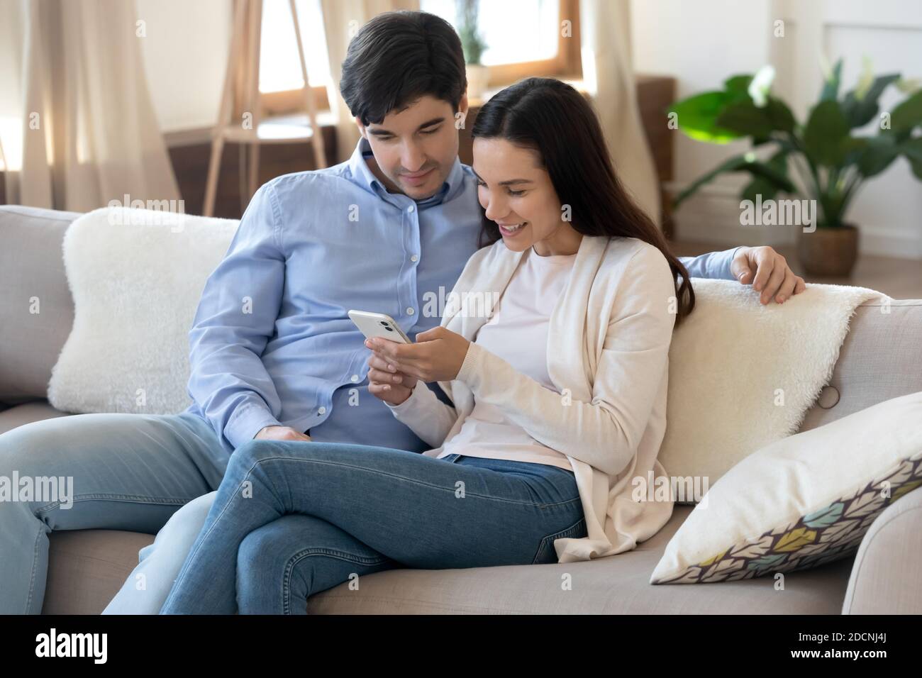 Glücklich liebende junge Familie Paar mit Handy auf der Couch Stockfoto