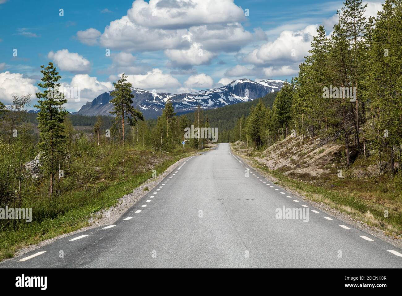 Schmale, einsame Straße durch die arktische Wildnis Lapplands, Schweden, die Jokkmokk und Kvikkjokk mit einer zerklüfteten, schneebedeckten Bergkette verbindet. Stockfoto